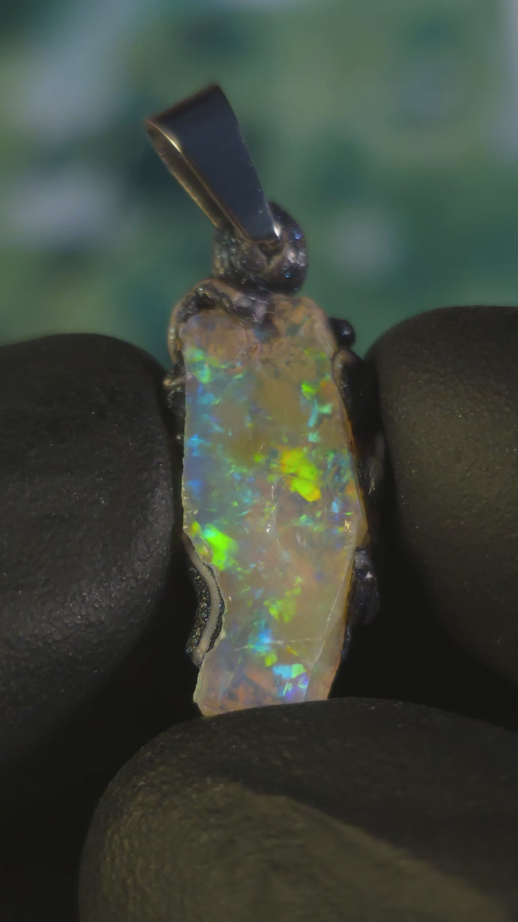 Video: raw uncut Ethiopian Welo opal pendant. Colour: blue and green, vivid. Body: transparent. Held in a gloved hand against a dark background.