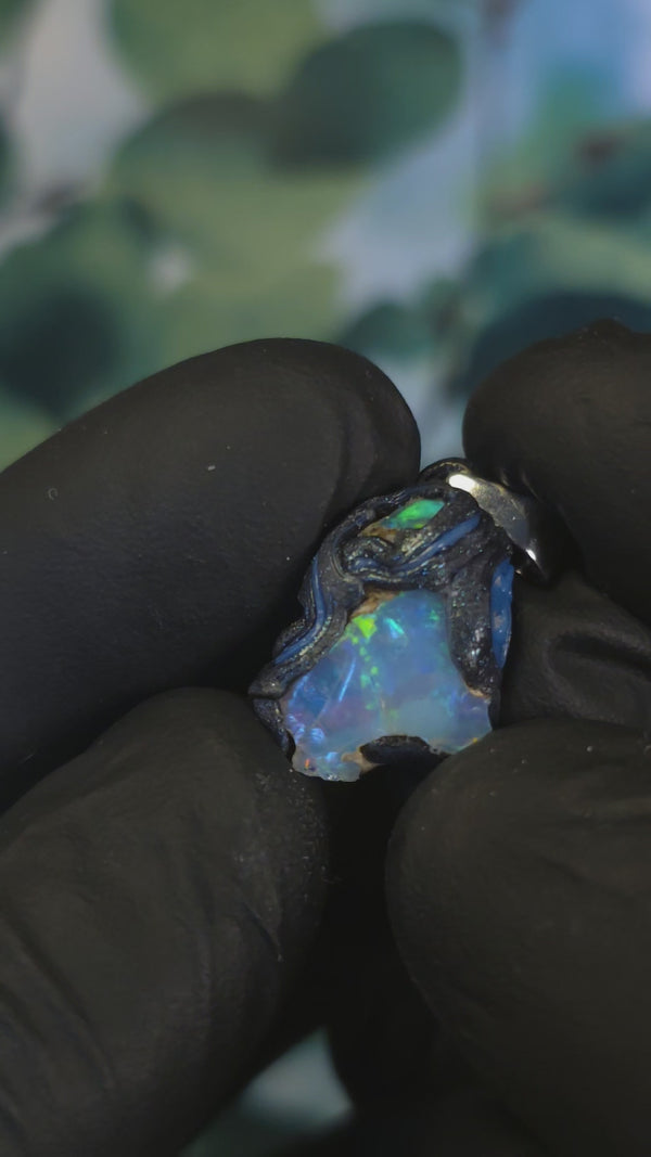 Video: raw uncut Ethiopian Welo opal pendant. Colour: green, blue, vivid. Body: blue. Held in a gloved hand against a green background.