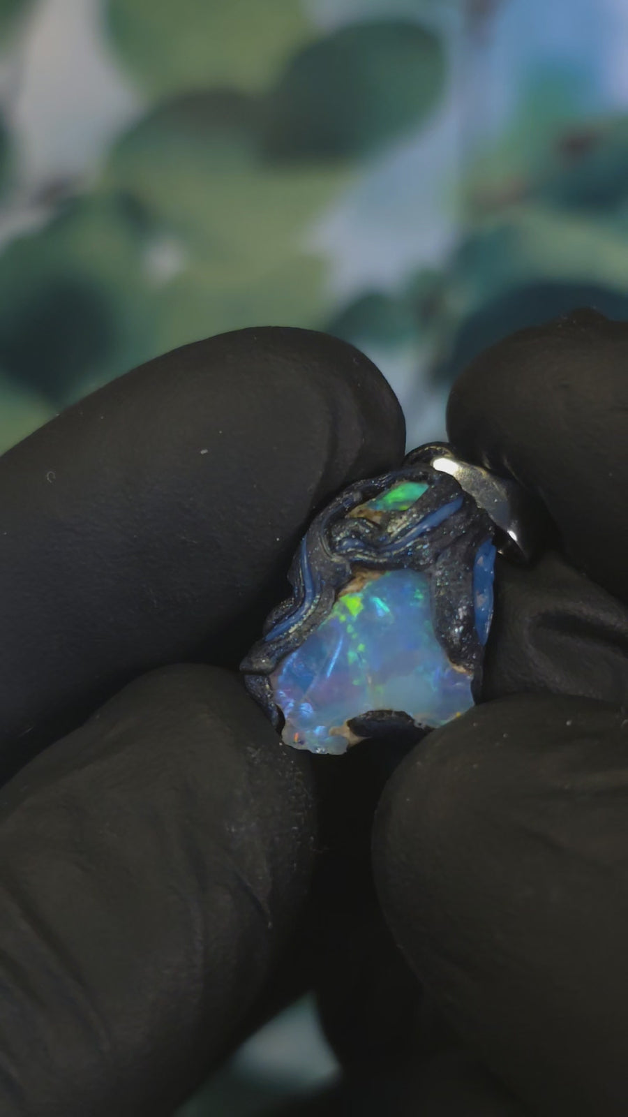 Video: raw uncut Ethiopian Welo opal pendant. Colour: green, blue, vivid. Body: blue. Held in a gloved hand against a green background.