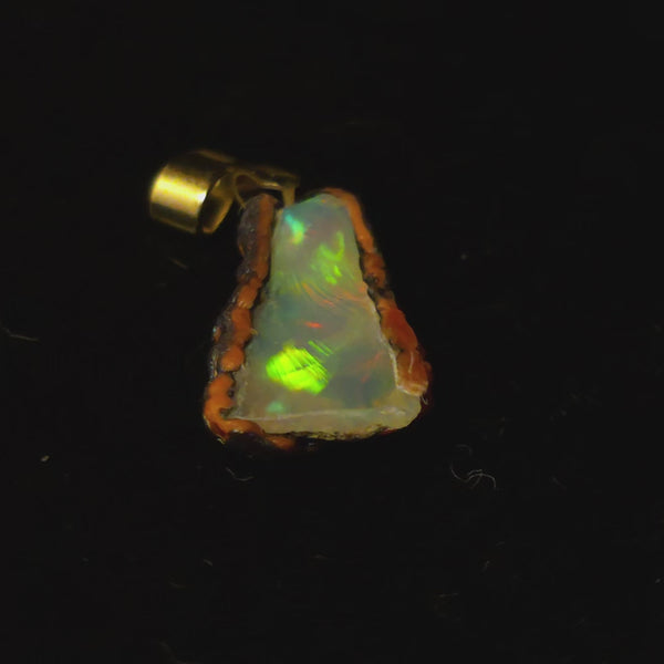 Video: raw uncut Ethiopian Welo opal pendant. Colour: green leading, red cutting in, blue at the edges, strong. Body: crystal clear. Lying on a dark surface.
