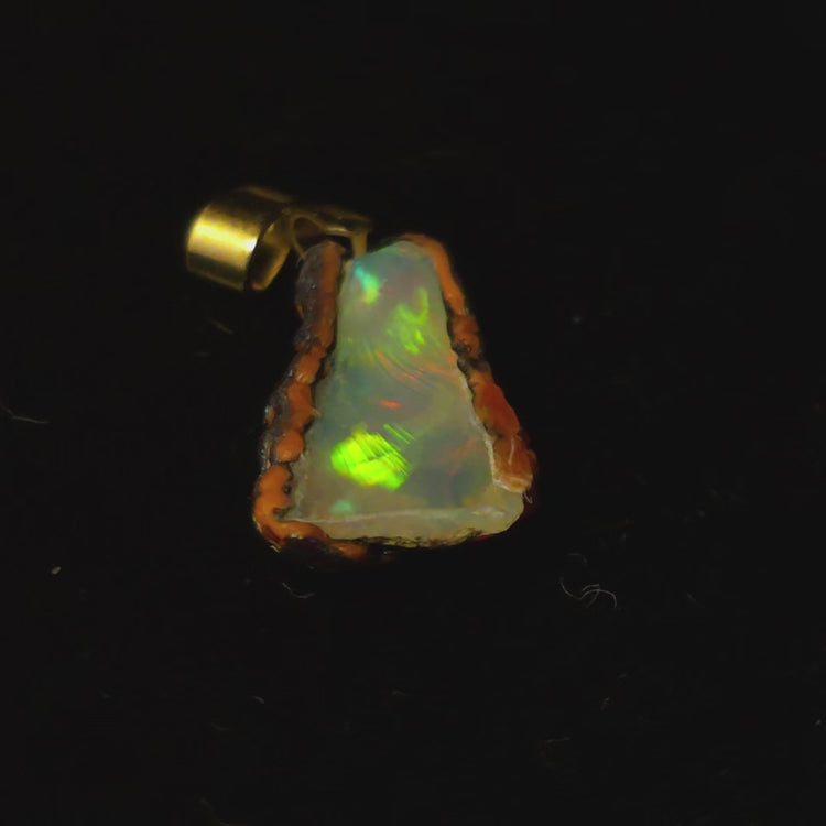 Video: raw uncut Ethiopian Welo opal pendant. Colour: green leading, red cutting in, blue at the edges, strong. Body: crystal clear. Lying on a dark surface.