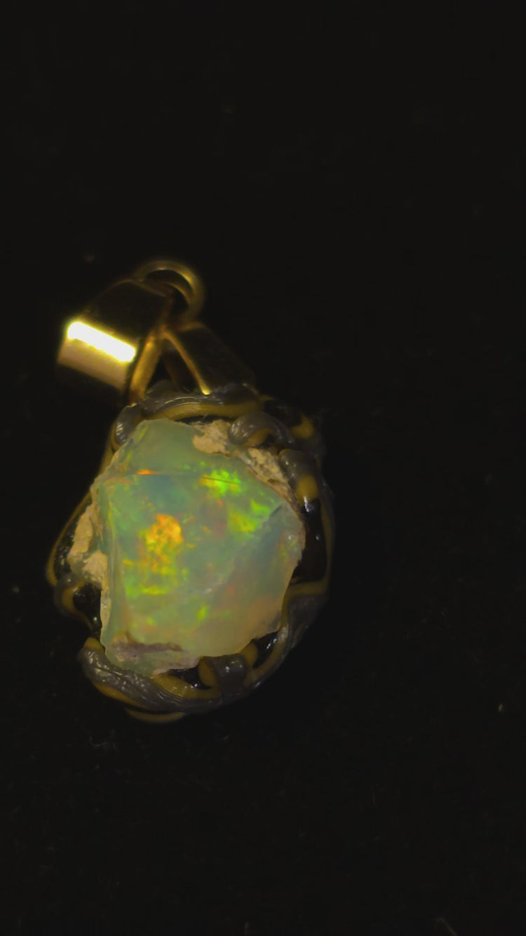 Video: raw uncut Ethiopian Welo opal pendant. Colour: green and red, strong. Body: light blue. Lying on a dark surface.