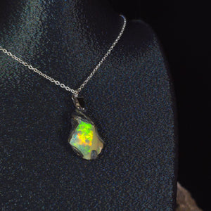 Raw uncut Ethiopian Welo opal pendant. Colour: blue, red, with green and yellow accents, vivid. Body: white. Worn on a black display bust.