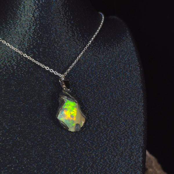 Raw uncut Ethiopian Welo opal pendant. Colour: blue, red, with green and yellow accents, vivid. Body: white. Worn on a black display bust.
