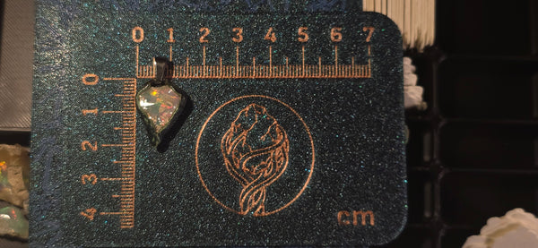 Raw uncut Ethiopian Welo opal pendant. Colour: red, green, vivid. Body: duotone blue/white. Placed next to a steel ruler for scale.