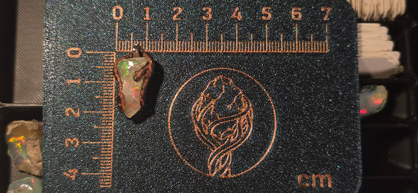Raw uncut Ethiopian Welo opal pendant. Colour: green, red, vivid. Body: white. Placed next to a steel ruler for scale.