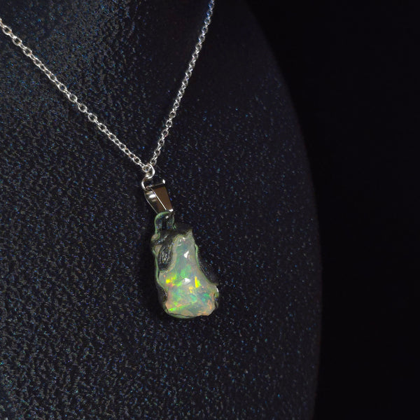 Raw uncut Ethiopian Welo opal pendant. Colour: green, blue-green, with red hints, vivid. Body: white. Worn on a black display bust.
