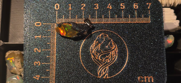 Raw uncut Ethiopian Welo opal pendant. Colour: red and orange, with a hint of green, vivid. Body: dark brown. Placed next to a steel ruler for scale.