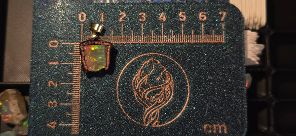 Raw uncut Ethiopian Welo opal pendant. Colour: green, gold, red, full rainbow, vivid. Body: dark. Placed next to a steel ruler for scale.