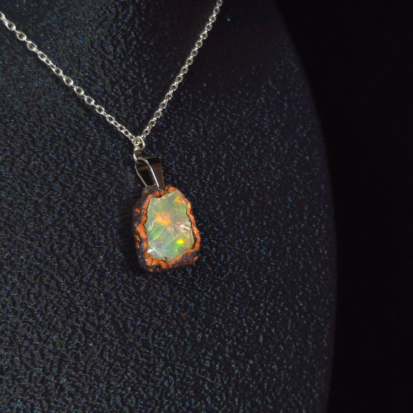 Raw uncut Ethiopian Welo opal pendant. Colour: red, green and gold, moderate. Body: clear with hazy surface. Worn on a black display bust.