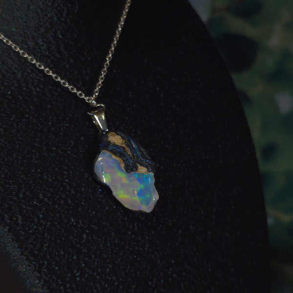 Raw uncut Ethiopian Welo opal pendant. Colour: blue, teal, with green hints, moderate. Body: light blue. Worn on a black display bust.