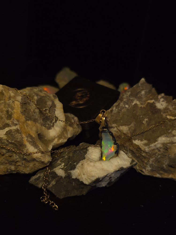Raw uncut Ethiopian Welo opal pendant, green flashes on light blue. Resting on rough rock.