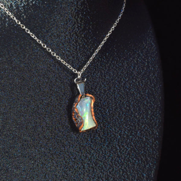 Raw uncut Ethiopian Welo opal pendant. Colour: red, gold with blue undertones, strong. Body: cloudy. Worn on a black display bust.