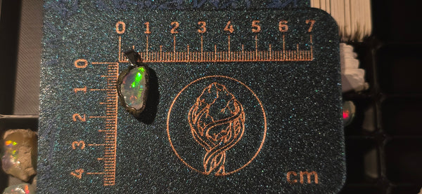 Raw uncut Ethiopian Welo opal pendant. Colour: green, orange, red, vivid. Body: very light blue. Placed next to a steel ruler for scale.