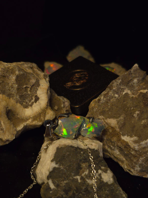 Raw uncut Ethiopian Welo opal pendant, shifting rainbow fire. Resting on rough rock.