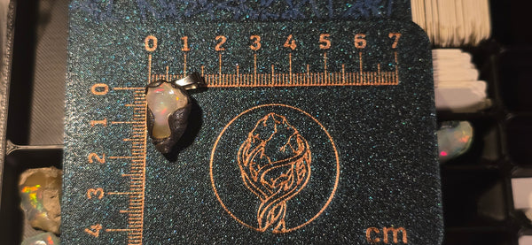 Raw uncut Ethiopian Welo opal pendant. Colour: gold, red, with green accents, vivid. Body: clear with white centre. Placed next to a steel ruler for scale.
