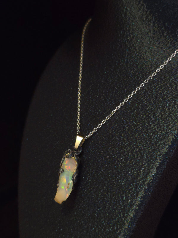 Raw uncut Ethiopian Welo opal pendant, rainbow flashes & red fire. Worn on a black display bust.