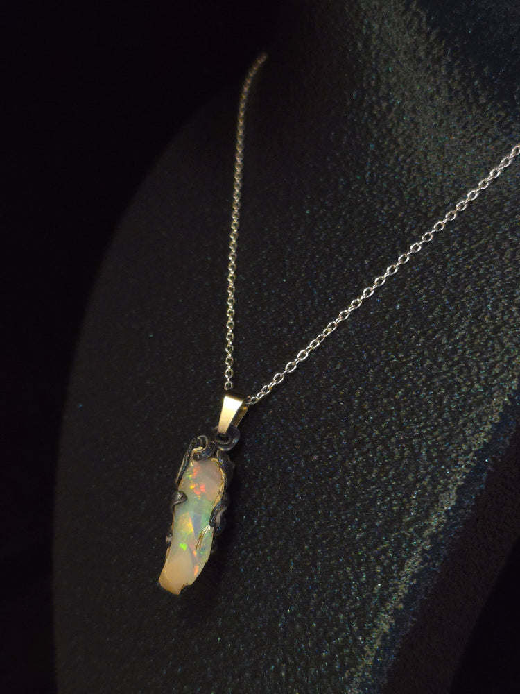 Raw uncut Ethiopian Welo opal pendant, rainbow flashes & red fire. Worn on a black display bust.