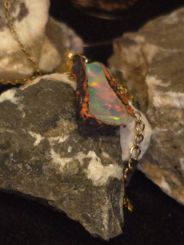 Raw uncut Ethiopian Welo opal pendant. Colour: green leading, red cutting in, blue at the edges, strong. Body: crystal clear. Resting on rough rock.