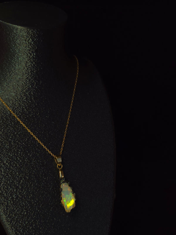 Raw uncut Ethiopian Welo opal pendant, green flashes on light blue. Worn on a black display bust.