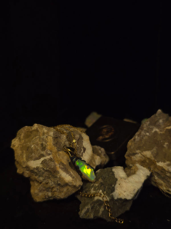 Raw uncut Ethiopian Welo opal pendant, green flashes on light blue. Resting on rough rock.