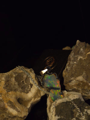 Raw uncut Ethiopian Welo opal pendant, shifting rainbow fire. Resting on rough rock.