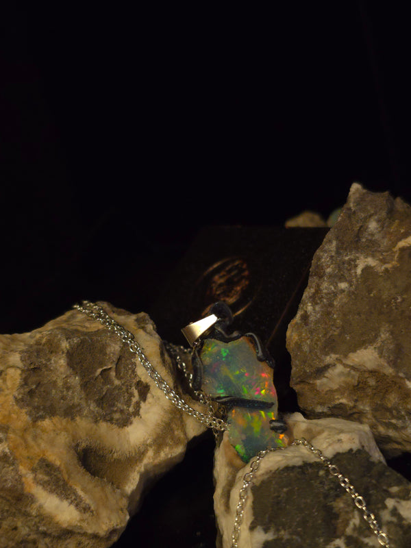 Raw uncut Ethiopian Welo opal pendant, shifting rainbow fire. Resting on rough rock.