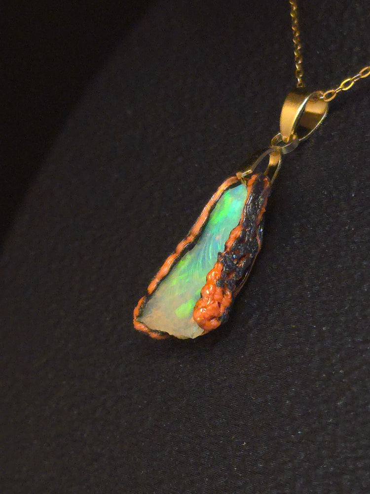 Video: raw uncut Ethiopian Welo opal pendant. Colour: green leading, red cutting in, blue at the edges, strong. Body: crystal clear. Lying on a dark surface.