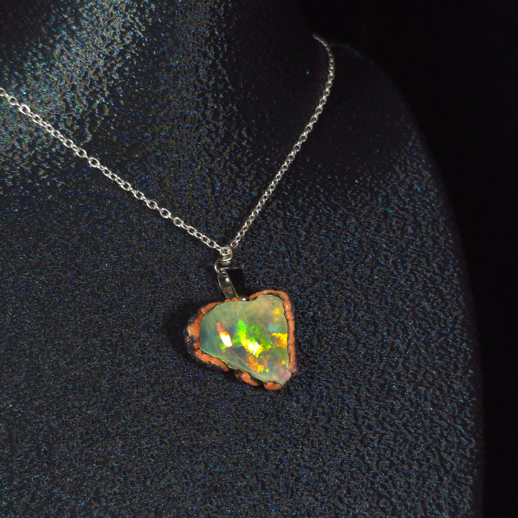 Raw uncut Ethiopian Welo opal pendant. Colour: full rainbow, vivid. Body: dark. Worn on a black display bust.