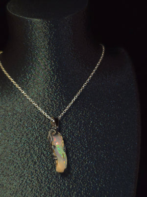 Raw uncut Ethiopian Welo opal pendant, rainbow flashes & red fire. Worn on a black display bust.