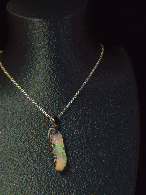 Raw uncut Ethiopian Welo opal pendant, rainbow flashes & red fire. Worn on a black display bust.