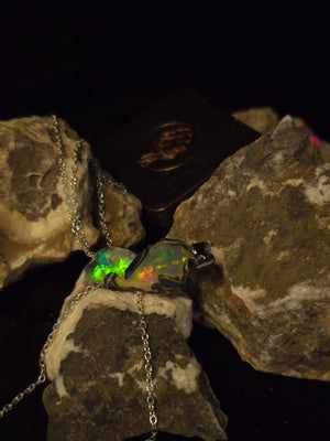 Raw uncut Ethiopian Welo opal pendant, shifting rainbow fire. Resting on rough rock.