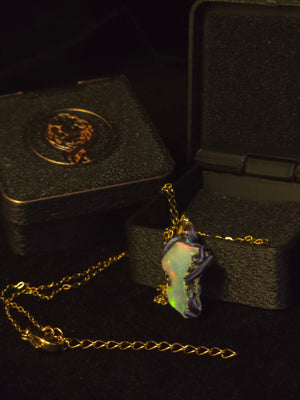 Raw uncut Ethiopian Welo opal pendant, every colour at once, blue body. Shown with its open gift box.