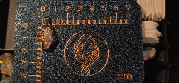 Raw uncut Ethiopian Welo opal pendant. Colour: red and green, strong. Body: crystal clear. Placed next to a steel ruler for scale.