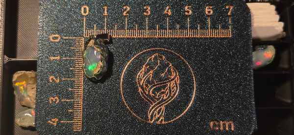 Raw uncut Ethiopian Welo opal pendant. Colour: green and blue, strong. Body: clear, light blue. Placed next to a steel ruler for scale.