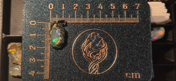 Raw uncut Ethiopian Welo opal pendant. Colour: green and blue, strong. Body: clear, light blue. Placed next to a steel ruler for scale.