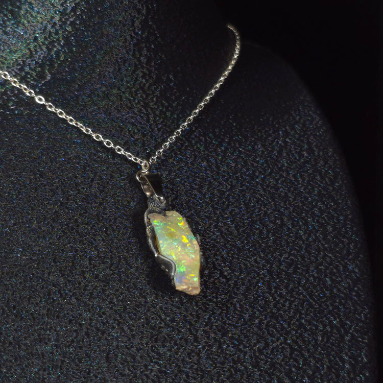 Raw uncut Ethiopian Welo opal pendant. Colour: blue and green, vivid. Body: transparent. Worn on a black display bust.